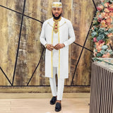 Man in a white traditional outfit with gold accents standing in front of a decorative wall with flowers.